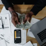 Proses perhitungan keuangan bisnis dengan kalkulator dan laptop di meja kerja